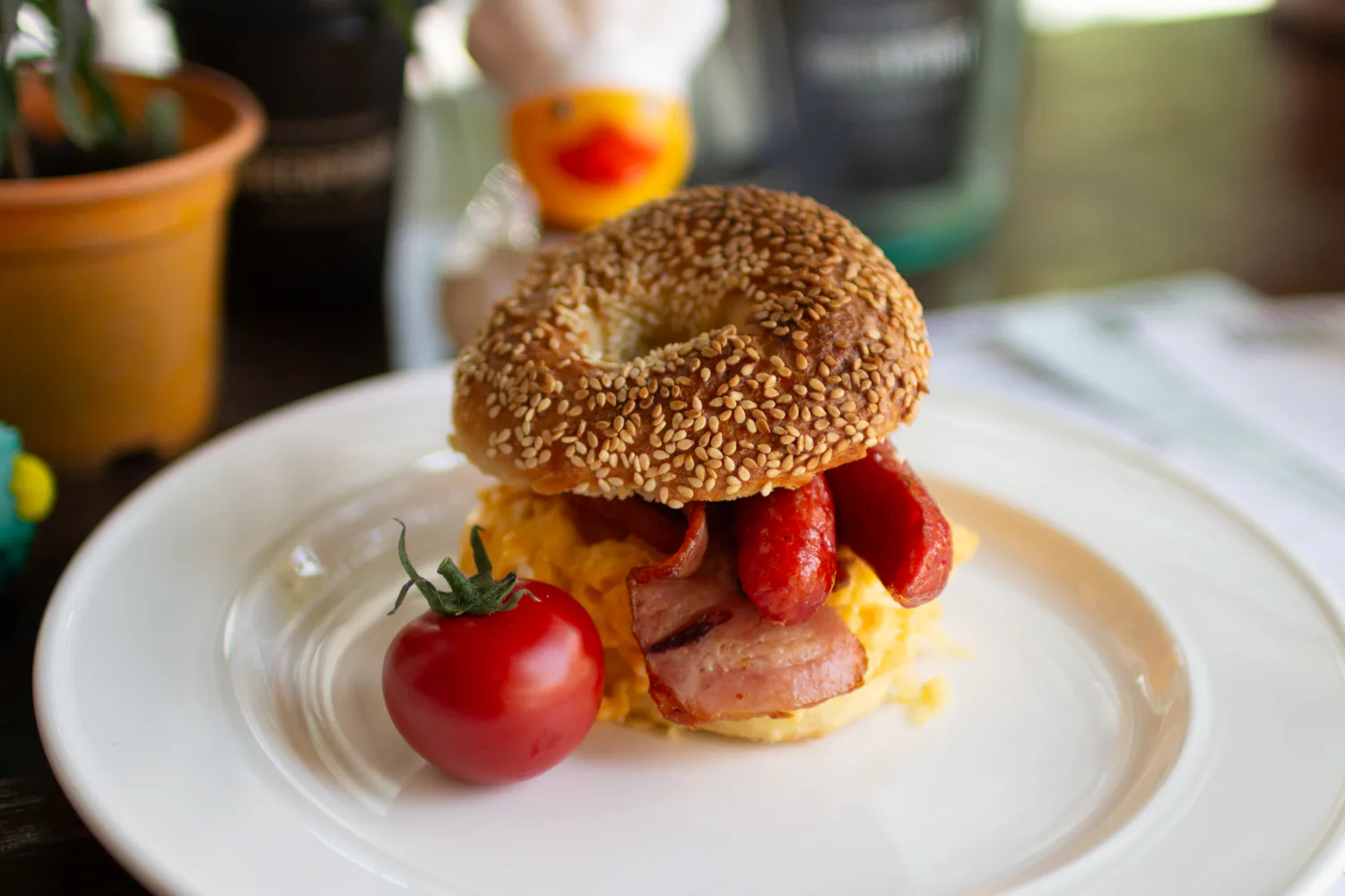Bagel with bacon, scrambled eggs, sausage, and tomato